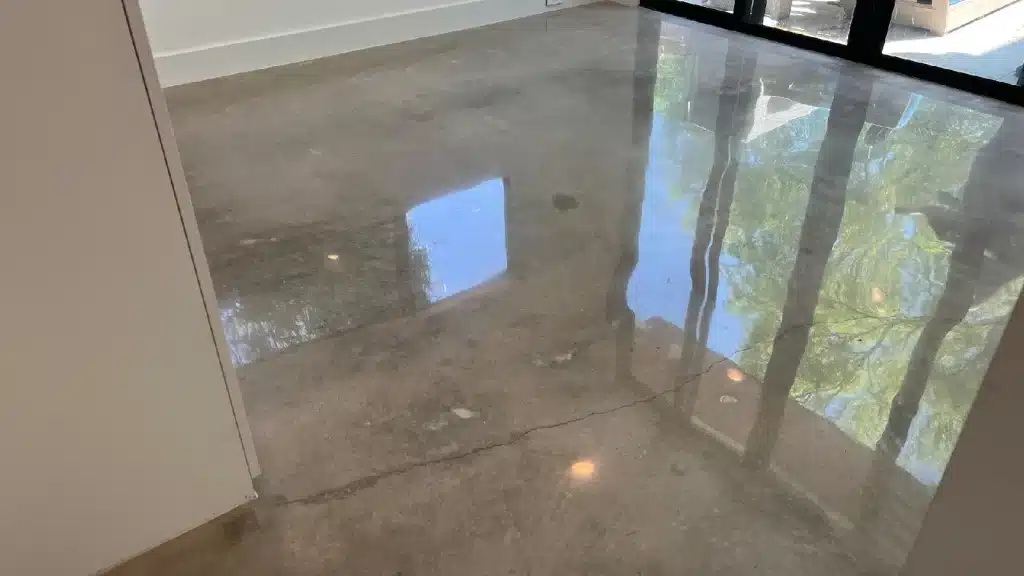 After concrete floor polishing showing a uniform reflective finish in a residential game room with visible natural concrete variation and hairline crack.
