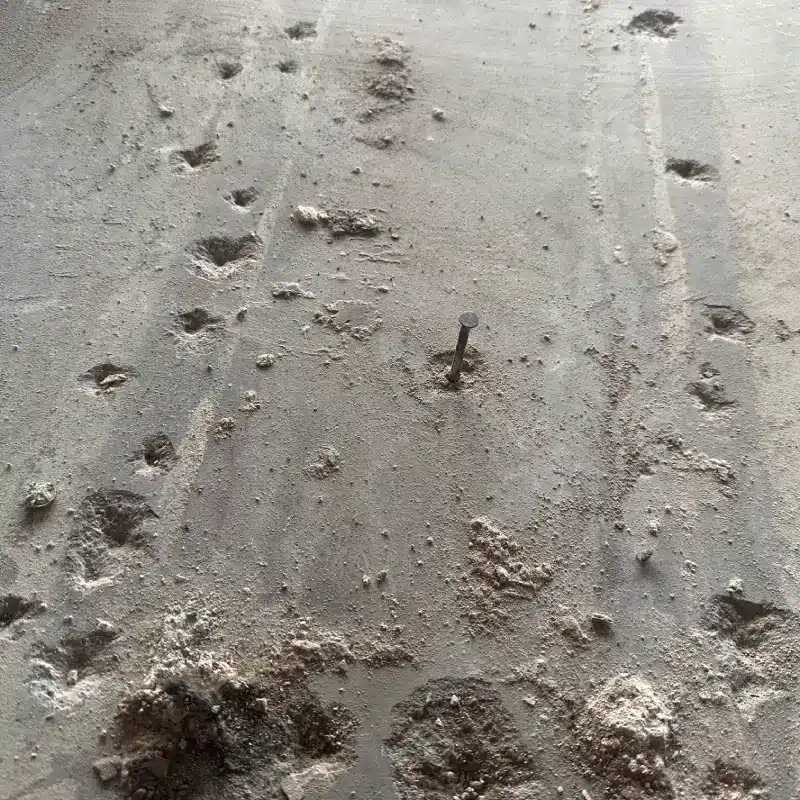 Concrete slab showing surface pitting, dusting, and embedded fasteners requiring floor prep assessment before installation