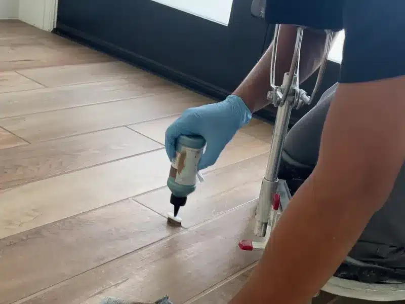 Technician applying grout color seal to wood-look tile floor for uniform color and long-lasting protection