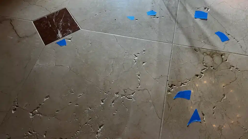 Marble floor before restoration showing surface pitting, voids, and visible damage.