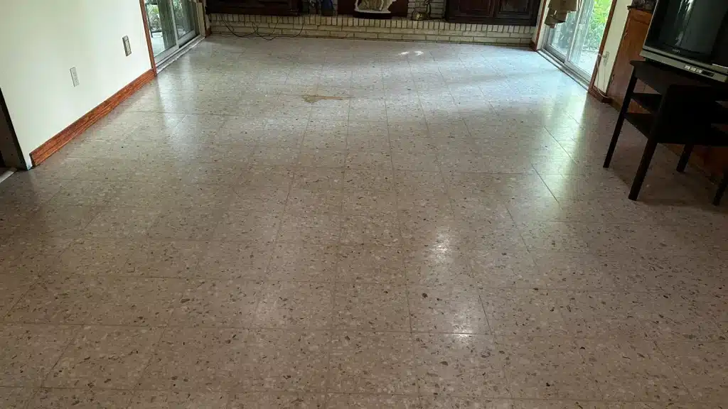 Terrazzo living room floor before restoration showing wax buildup, yellowing, and surface wear in Goliad, TX