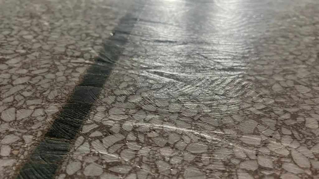 Close-up of terrazzo floor showing heavy grind marks and uneven surface damage before restoration in Downtown Houston, Texas.