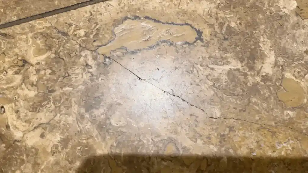 Travertine floor with visible cracks and open holes before lippage correction in League City TX