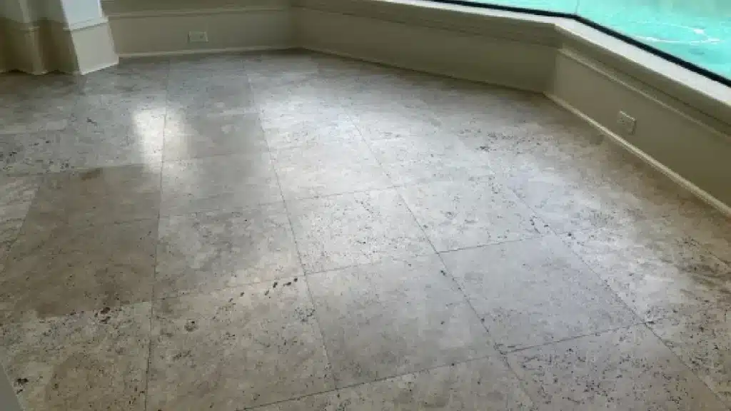 Travertine floor before polishing showing scratches, etching, and embedded soil in natural voids.