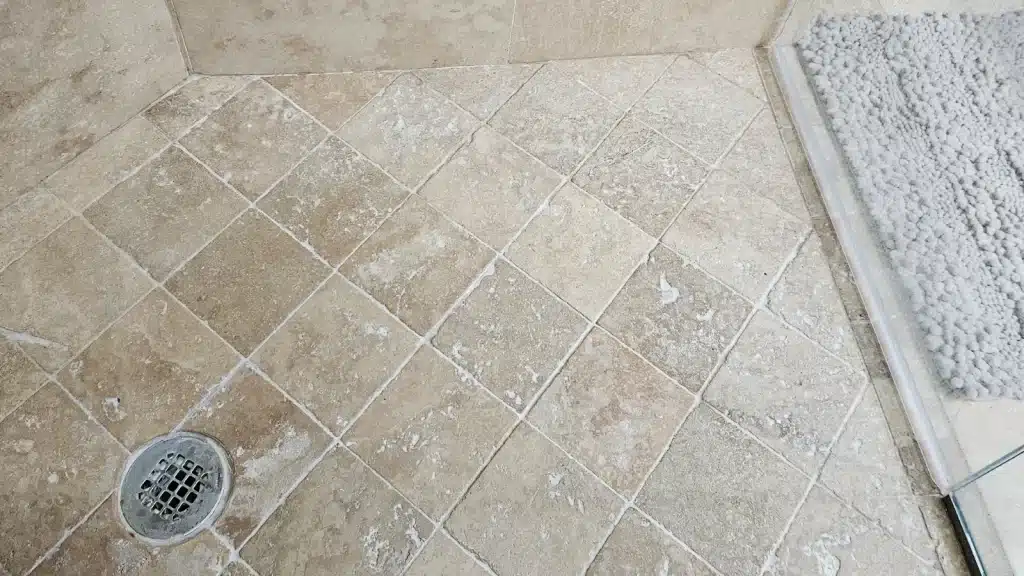 Travertine shower floor and walls showing bleach etching and mineral buildup