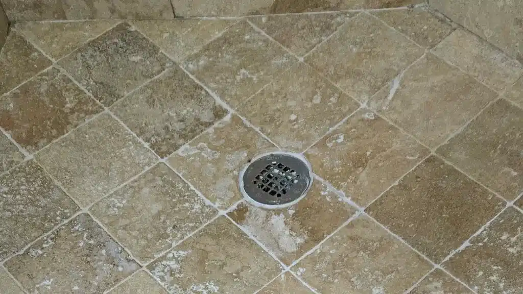 Bleach damage on travertine shower floor showing white etching and surface deterioration